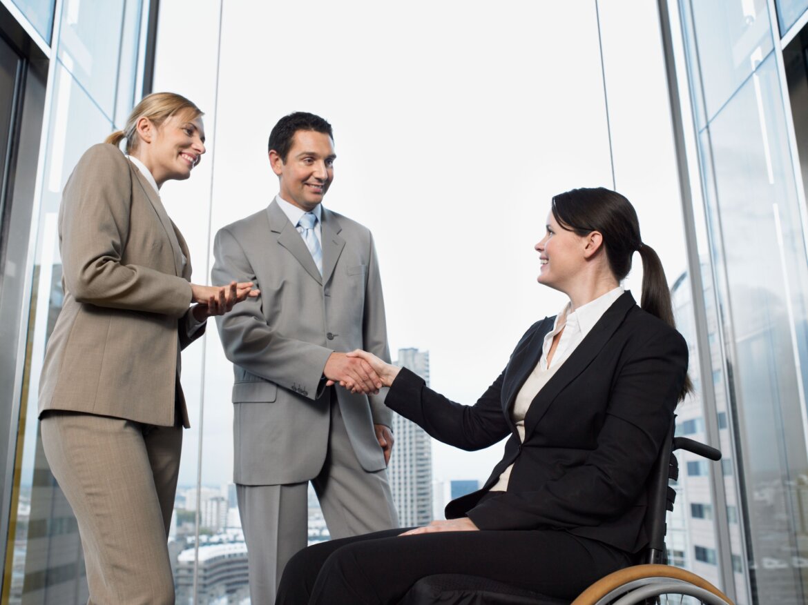 Lavoro e disabilità Donna disabile in ambiente di lavoro stringe la mano a colleghi