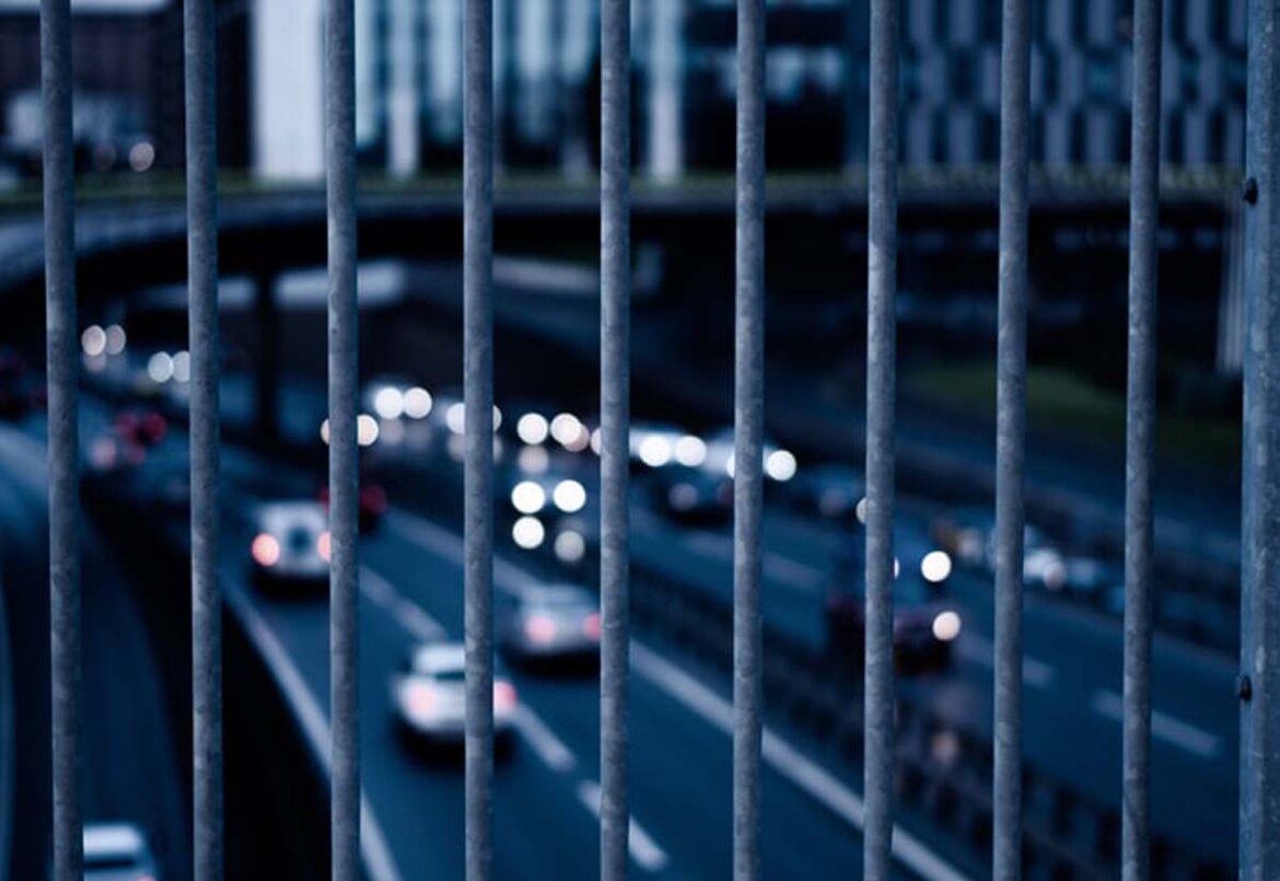 Veicoli su strada visti da lontano dietro sbarre di un cancello