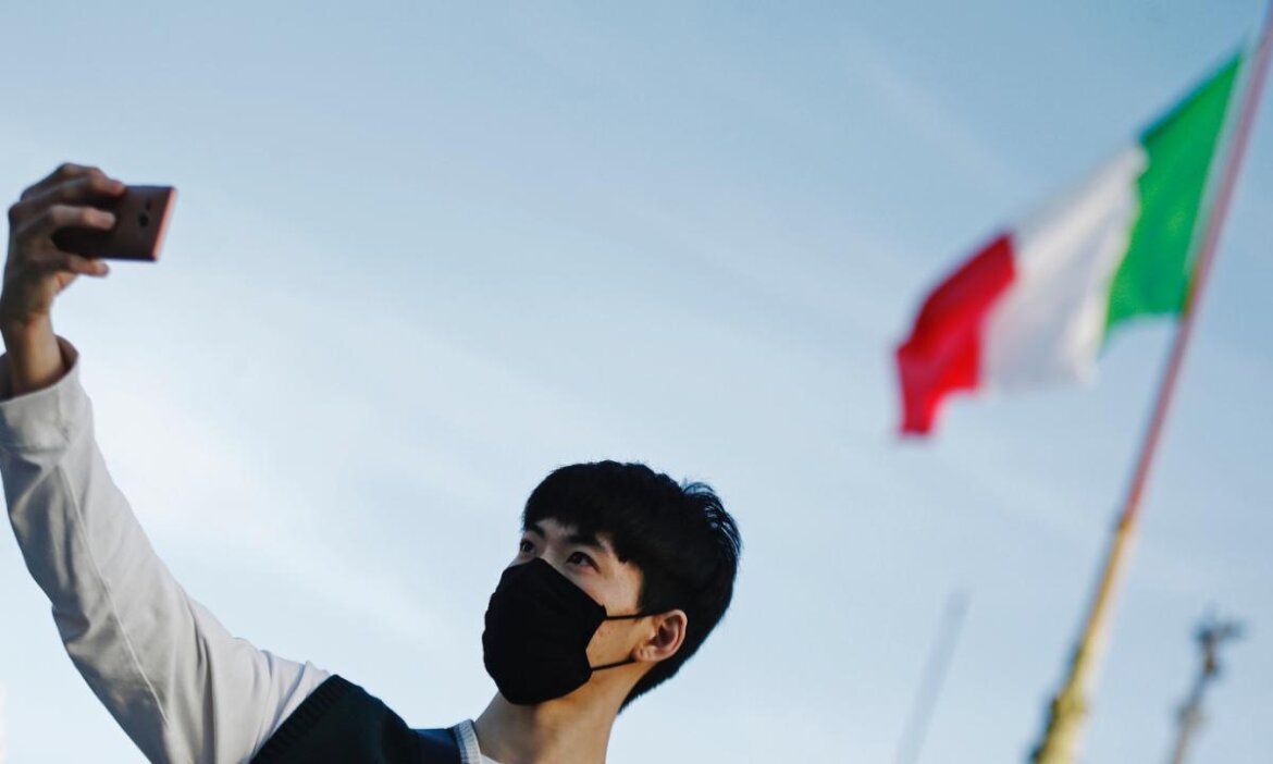 Turista con la mascherina si scatta una foto con dietro il Tricolore italiano
