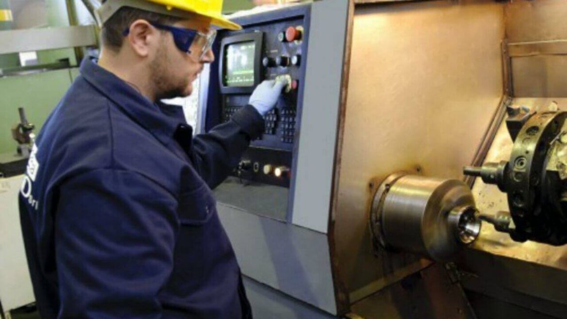 operaio con casco che lavora davanti ad un macchinario