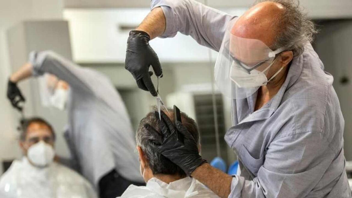 Parrucchiere con visiera e mascherina mentre taglia i capelli